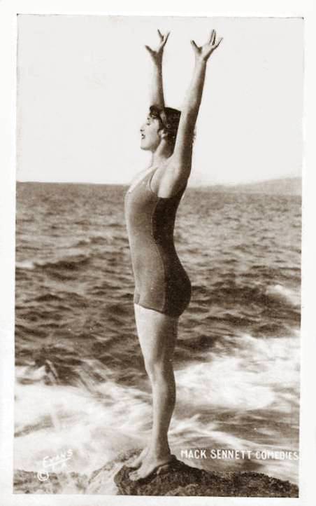 arcade-card-mack-sennett-comedies-woman-in-wooly-bathing-suit-standing-on-rock-with-arms-up1