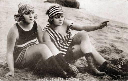 arcade-card-mack-sennett-comedies-two-women-sitting-on-beach-with-head-wraps-and-tall-boots-one-pointing