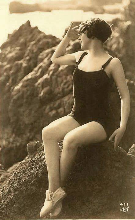 arcade-card-french-woman-in-bathing-suit-on-rocks-looking-to-sea-and-shading-her-eyes-1920s