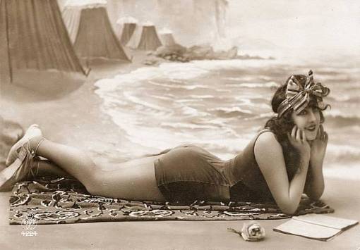 photo-for-arcade-card-woman-lying-with-head-up-on-forearms-swimsuit-and-large-bow-headdress-on-beach-set