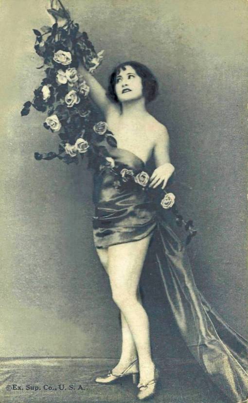 arcade-card-exhibit-supply-company-pin-up-woman-standing-in-satin-wrap-with-long-bough-of-roses-1920s