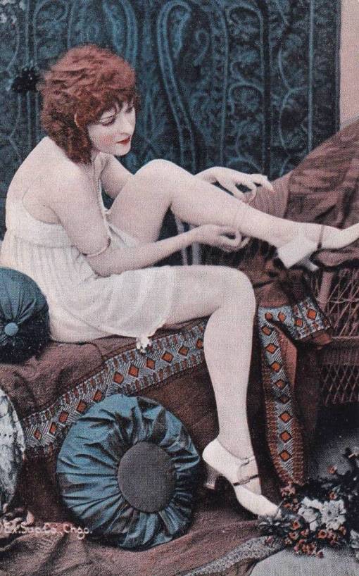 ARCADE CARD - EXHIBIT SUPPLY COMPANY - PIN UP - RED-HEADED WOMAN IN NIGHTIE AND HIGH HEELASON SETTEE WITH LEG UP ADJUSTING HOSE - TINTED - 1920s