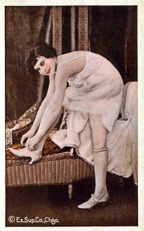 ARCADE CARD - EXHIBIT SUPPLY COMPANY - PIN UP - WOMAN IN NIGHTIE BUCKLING HER SHOE ON A SETTEE AND TURNED TO SMILE AT THE CAMERA - TINTED - 1920s