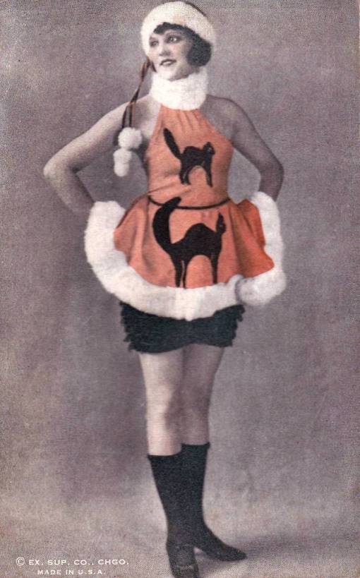 ARCADE CARD - EXHIBIT SUPPLY COMPANY - WOMAN STANDING WITH HANDS ON HIPS WEARING A BIZARRE COSTUME THAT RESEMBLES A BLEND OF HALLOWEEN AND CHRISTMAS - TINTED - 1920s