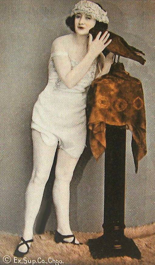 A ARCADE CARD - EXHIBIT SUPPLY COMPANY - PIN UP - WOMAN IN A SLIP AND LACEY HEADBAND STANDING BY AND PETTING A STUFFED BIRD - TINTED - 1920s