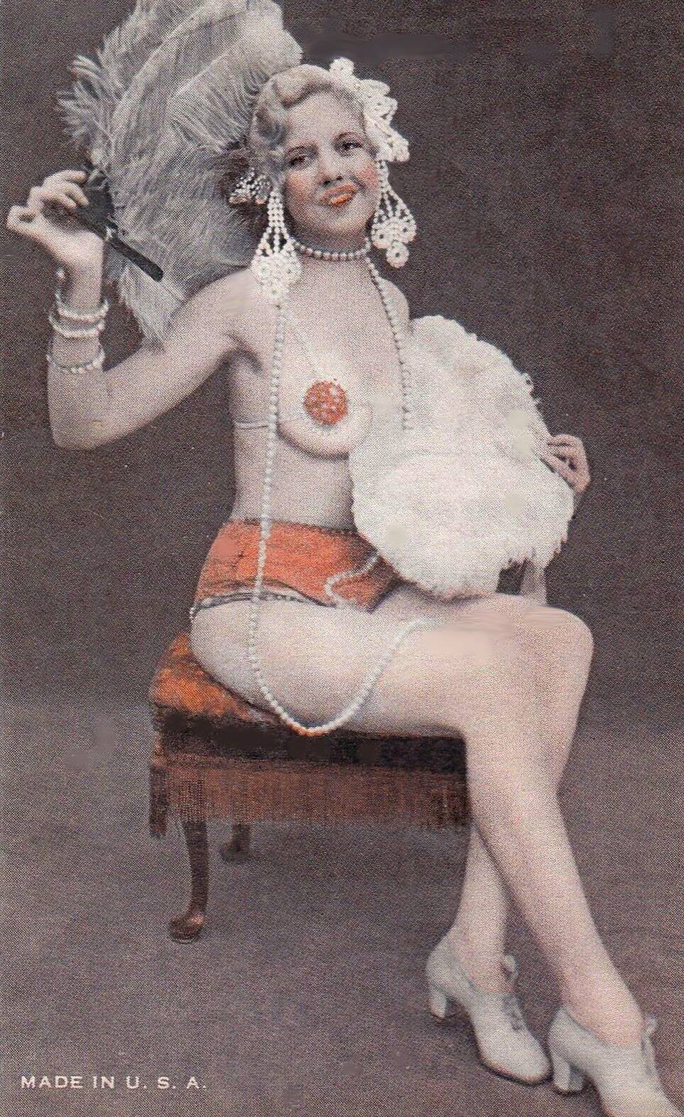 ARCADE CARD - EXHIBIT SUPPLY COMPANY - WOMEN IN TWO PIECE SMALL OUTFIT AND BIG FEATHERED HEADDRESS AND STRANDS OF PEARLS SITTING ON A CHAIR SMILING AT CAMERA - TINTED - 1920s